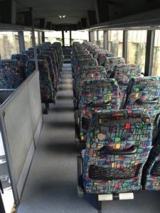 Upper level of double decker bus, rows of refurbished seats backs with grab handles and magazine pockets
