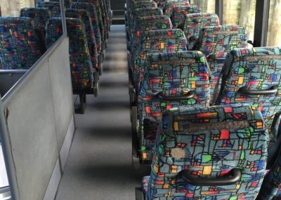 Upper level of double decker bus, rows of refurbished seats backs with grab handles and magazine pockets