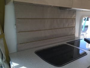 Beige coloured roman blind pulled down in motorhome behind kitchen bench in motohome