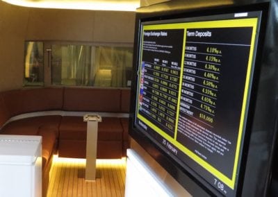 Interior of mobile unit for financial institution. Features a u shaped seat in tan trim in background and TV screen with financial metrics in foreground