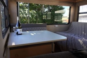 Finished interior of motorhome with eating and bedding areas upholstered in a soft grey with pattered geometric grey and white accent
