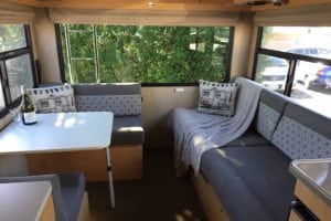 Finished interior of motorhome with eating and bedding areas upholstered in a soft grey with pattered geometric grey and white accent