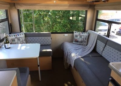 Finished interior of motorhome with eating and bedding areas upholstered in a soft grey with pattered geometric grey and white accent