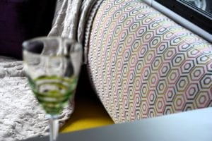 Grey, pink, yellow white geometric patterned cushion draped with a grey luxury throw