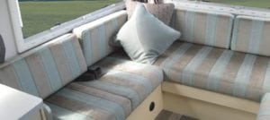 Motorhome seating in grey and blue stripe. Grey throw cushion sits in corner. Grass in background through window