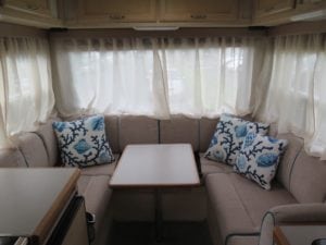 Motorhome in beige with turquoise piped cushions with table in the centre. Blue and white sea themed throw cushions