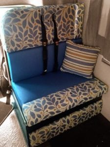 Motorhome passenger seat in royal blue accented by a yellow, blue and white leaf pattern. Shown with seatbelts and yellow, blue and white throw cushion.