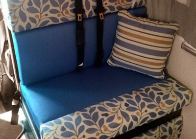 Motorhome passenger seat in royal blue accented by a yellow, blue and white leaf pattern. Shown with seatbelts and yellow, blue and white throw cushion.