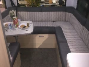 Motorhome interior trimmed in a grey and white geometric fabric with a charcoal accent. A dining table laid with plates, utensils, food and a vase of flowers.