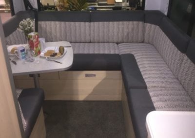 Motorhome interior trimmed in a grey and white geometric fabric with a charcoal accent. A dining table laid with plates, utensils, food and a vase of flowers.