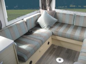 Motorhome seating in grey and blue stripe. Grey throw cushion sits in corner. Grass in background through window