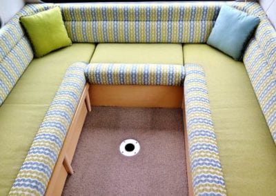 Motorhome interior with lime coloured base trim accented by a white, lime and blue geometric pattern. Throw pillows sit in each corner.