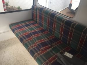 Large seat in caravan trimmed navy, green, red and white plaid. Charcoal fabric swatches are laid on top.