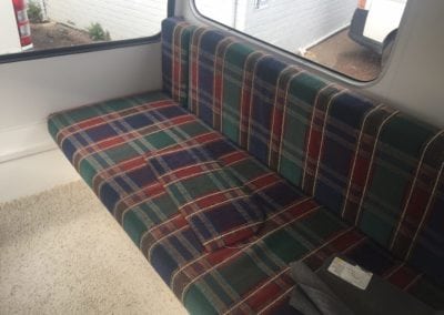 Large seat in caravan trimmed navy, green, red and white plaid. Charcoal fabric swatches are laid on top.