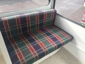 Seat trimmed in navy, green, red and white plaid before refurbishment in front of caravan windows