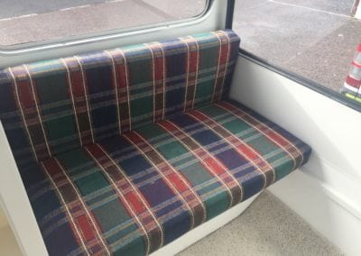 Seat trimmed in navy, green, red and white plaid before refurbishment in front of caravan windows