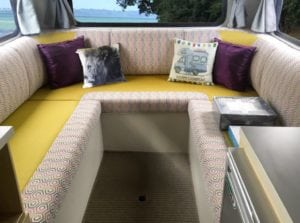 6 berth motorhome interior seating area upholstered in yellow with a grey, pink and white geometric patterned accent fabric