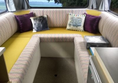 6 berth motorhome interior seating area upholstered in yellow with a grey, pink and white geometric patterned accent fabric