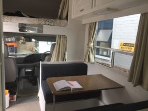 Front of motorhome showing drivers cabin and dining seating with table.