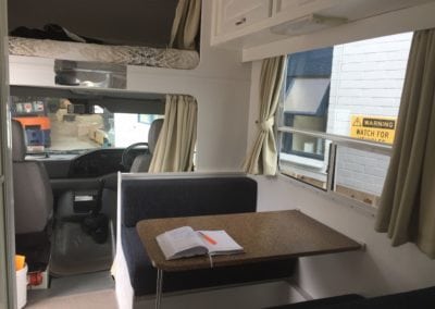 Front of motorhome showing drivers cabin and dining seating with table.