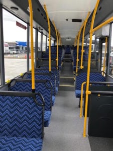 Interior of bus with blue chevron trimmed seats on either side of aisle up to the back of the bus