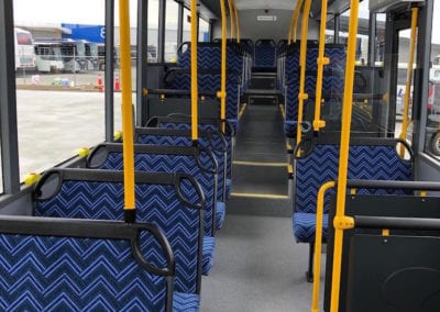 Interior of bus with blue chevron trimmed seats on either side of aisle up to the back of the bus