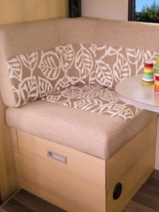 Corner dinette in beige and white leaf patterned fabric. Edge of table with dinnerware can be seen on right hand side of image.
