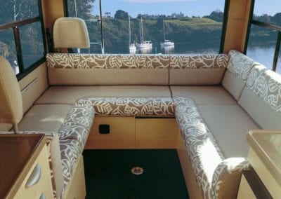 Motorhome lounge cushions in beige with leaf patterned edges. Water with boats are in the background through the rear window