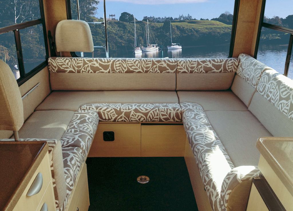 Motorhome lounge cushions in beige with leaf patterned edges. Water with boats are in the background through the rear window