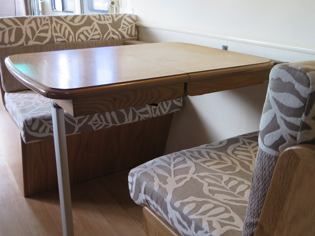 Front and Rear facing dinette with table in the middle. Upholstered in beige and white leaf pattered fabric.