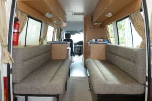 Rear view of walk through motorhome. Beige coloured cushions flank both sides of the vehicle. The drivers cabin can be seen in the background.