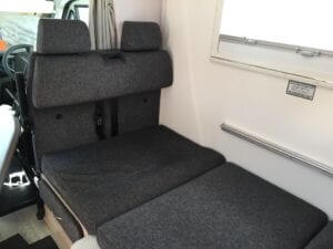 Dark grey passenger seating in motorhome in sleeping position. Drivers seat and steering wheel visible in background