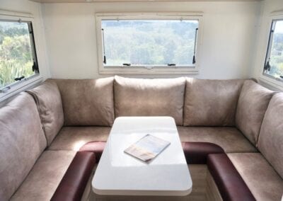 U shaped lounge with two tone seat cushions in brown and burgundy and plain brown seat cushions . White table with magazine in the middle and windows with greenery