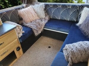Motorhome U shaped lounge with royal blue seat squabs and fan shaped cream pattern on royal blue background. Furry cushions and blankets adorn the seating.