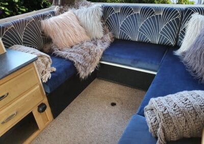 Motorhome U shaped lounge with royal blue seat squabs and fan shaped cream pattern on royal blue background. Furry cushions and blankets adorn the seating.