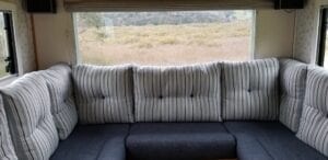 Motorhome U shaped lounge with striped feather and fibre filled back cushions and navy foam filled seat cushions. Grassy landscape in background through window.