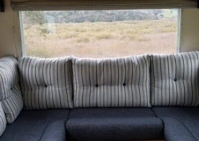 Motorhome U shaped lounge with striped feather and fibre filled back cushions and navy foam filled seat cushions. Grassy landscape in background through window.